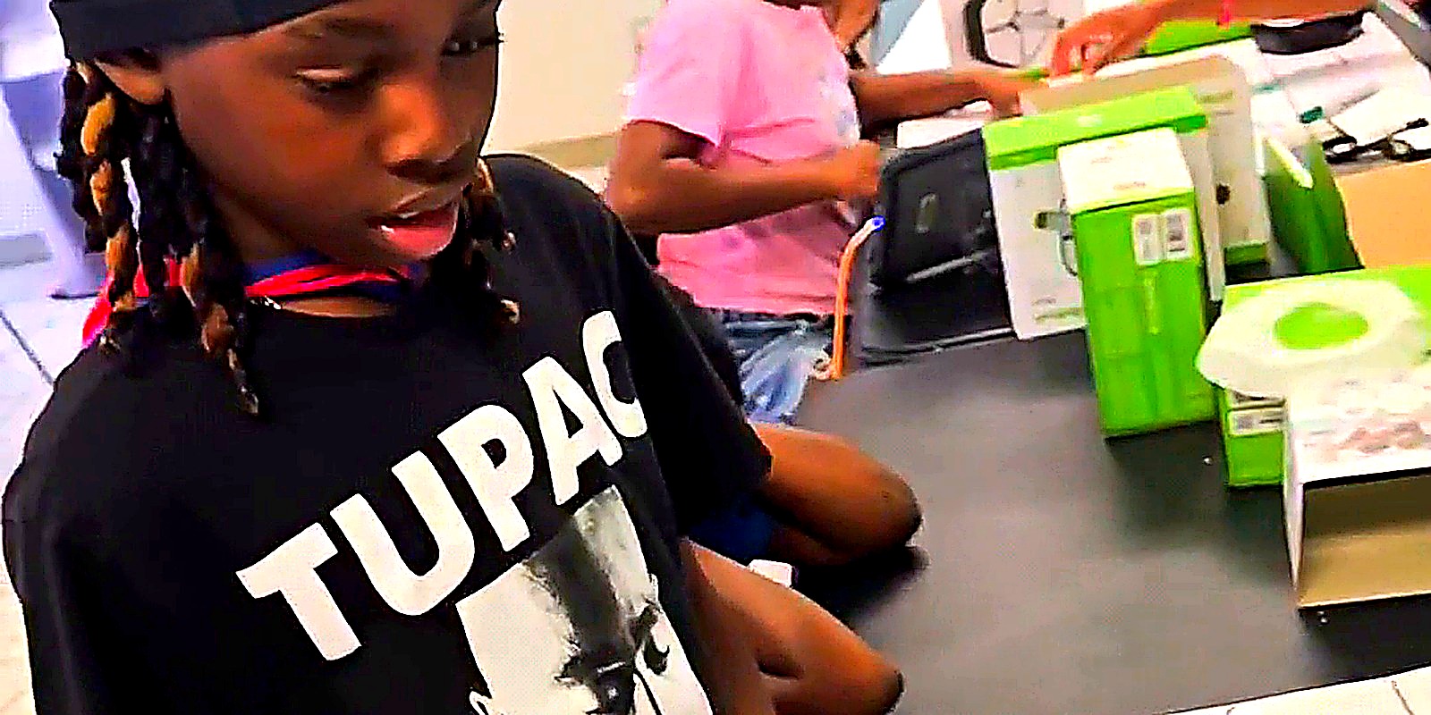 Students coding Root-style robots on a colorful carpet grid with laptops